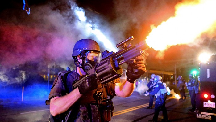 A member of the St. Louis County Police tactical team fires tear gas into a crowd of people in response to a series of gunshots fired at police during demonstrations in Ferguson, Missouri