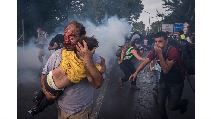 Un hombre trata de proteger a su hijo contra golpes de la policía y gases lacrimógenos en el cruce fronterizo en Horgoš, Serbia. Foto: Sergey Ponomarev/ The New York Times