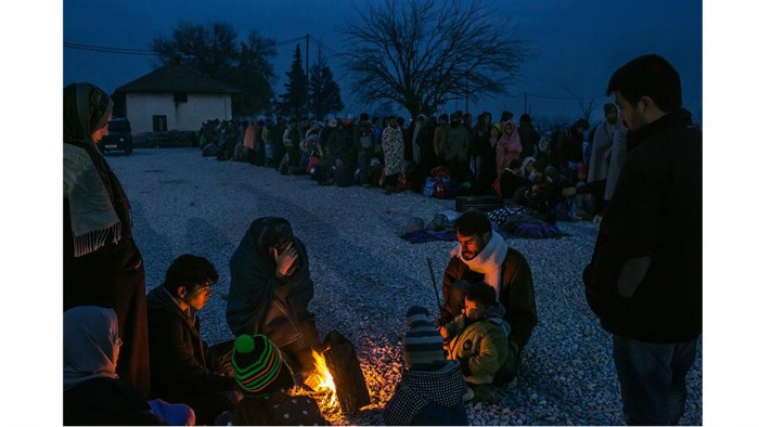 Una familia de refugiados de Siria se calienta alrededor de una fogata, como otros hacen cola para ser registrados en un campo de recepción, en Gevgelija, Macedonia. Foto: Mauricio Lima/ The New York Times