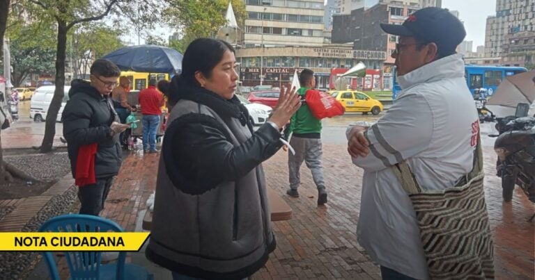 Two people talk on a busy city square: a woman gestures toward a man in a white jacket with a striped bag, with taxis and a bus in the background and a 'NOTA CIUDADANA' banner in view. - Así es como el lenguaje se deteriora entre redes sociales, eufemismos empresariales y la ausencia de lectura