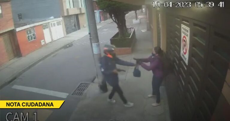 Surveillance still: a man in dark clothing reaches for a woman in a purple jacket on a sidewalk outside a building; timestamp 10-04-2023 05:39:41. - La justicia por mano propia se disparó en Bogotá ante la incapacidad de la Policía para atajar a los ladrones