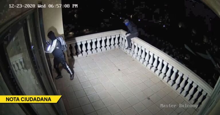 Nighttime security footage of two masked individuals with backpacks on a tiled balcony, one near a glass door appearing to force entry. - El drama de los abuelos gringos en Nueva York a quienes les están robando sus casas