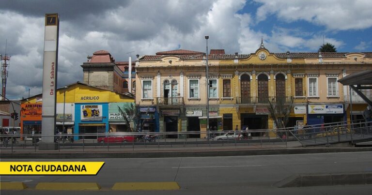 Colorful city street with colonial storefronts, signs, and a raised pedestrian walkway in front. - La Estación de La Sabana, un espacio desperdiciado que salvaría al centro de Bogotá