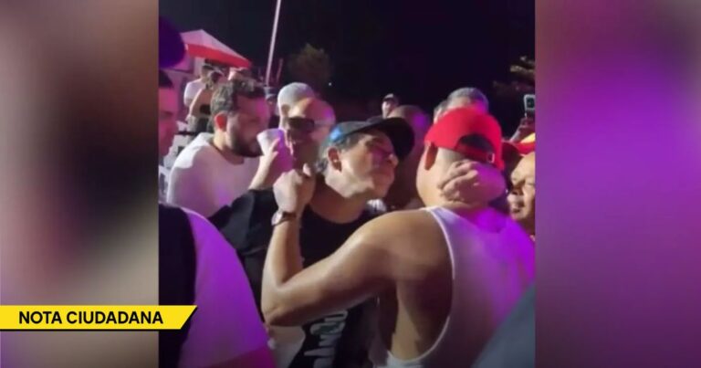 Two men embrace in a crowded nighttime scene with purple lighting and a yellow 'NOTA CIUDADANA' banner at the bottom. - El beso de Alejandro Char a Elder Dayán tiene a los barranquilleros pidiendo un examen psiquiátrico para su alcalde