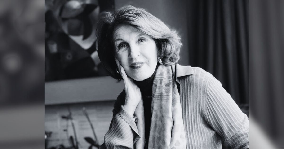 Black-and-white portrait of an older woman resting her head on her hand, looking at the camera with a gentle smile. - Cómo estimular la autoestima positiva en los hijos