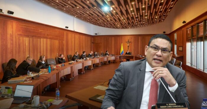 Formal parliamentary or council meeting in progress inside a wood-paneled chamber; a man in a suit speaks into a microphone at the foreground while other officials sit around a curved table in the background. - Las2orillas.co: Historias, voces y noticias de Colombia