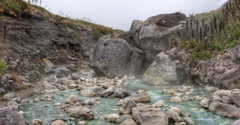 Geothermal stream with milky turquoise water surrounded by large rocks and rocky hills, steam rising. - Así puede llegar al único río de aguas calientes color turquesa en Colombia, una joya natural en el Tolima