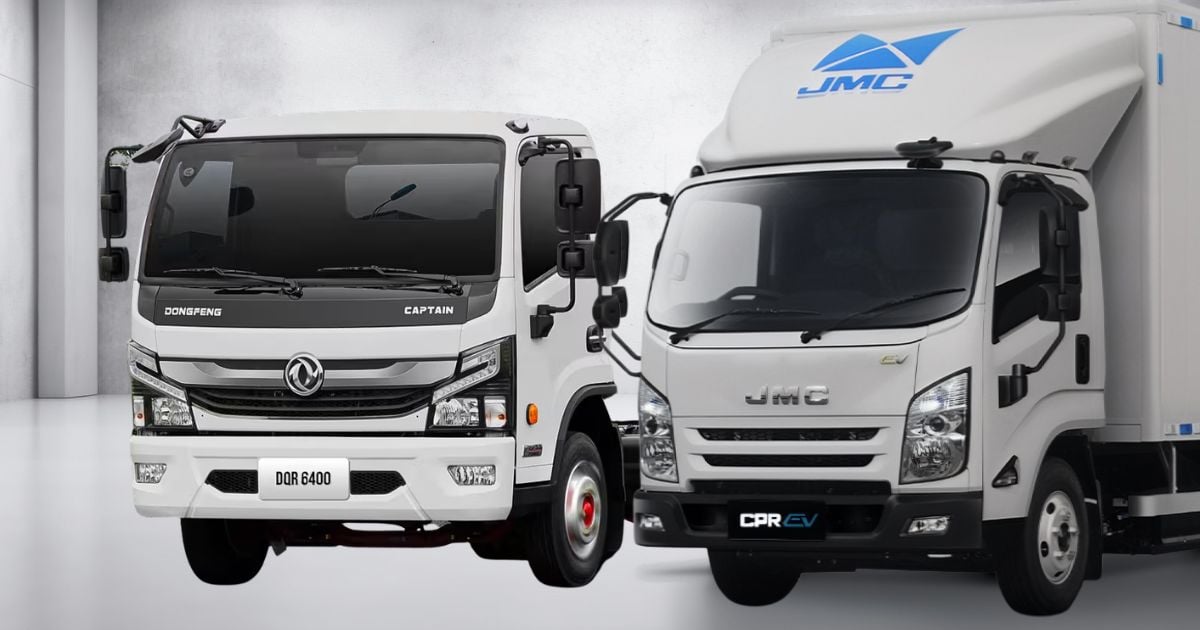 Two white delivery trucks parked side by side in a showroom, front views visible (Dongfeng Captain and JMC models). - La revolución silenciosa de las marcas chinas: cómo el gas y la electricidad vencieron al diésel en la montaña