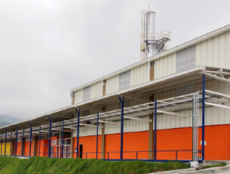 Exterior of a large industrial warehouse with orange walls and blue support columns under a metal roof, with an antenna on top. - La repostería Deli le ganó a una multinacional China