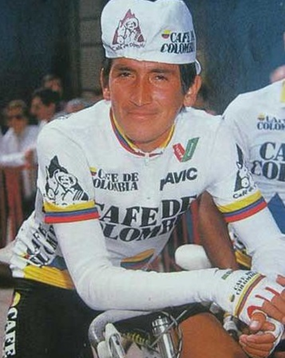 Professional cyclist in a white Café de Colombia team jersey and cap, resting on a bicycle during a race installment. - La jugada de Germán Bahamón para traer de vuelta Café de Colombia con equipo de ciclismo de talla mundial