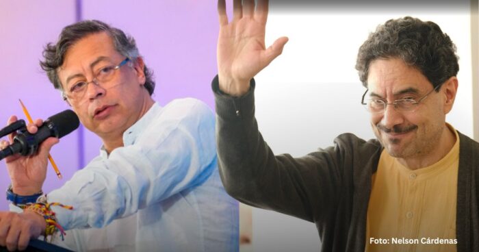 Two men speaking on stage: left man at a microphone with a pencil in hand, right man raising his hand and smiling. - Las2orillas.co: Historias, voces y noticias de Colombia