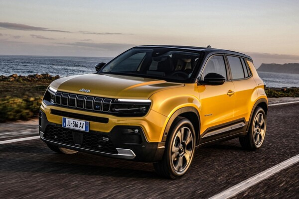 Yellow Jeep Grand Cherokee SUV driving along a coastal highway at sunset, ocean on the left and rocky shore in the distance. - La guerra de los carros eléctricos en Colombia puso a varias marcas a bajar los precios de sus modelos