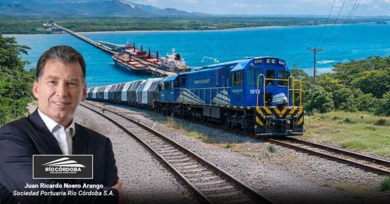 Portrait of Juan Ricardo Noero Arango, executive of Sociedad Portuaria Río Córdoba, standing beside a blue cargo train near a coastal port with ships in the background. - Las2orillas.co: Historias, voces y noticias de Colombia