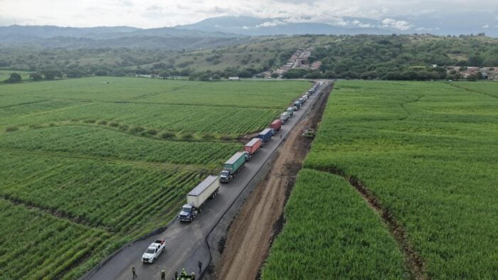 De dos islas del Caribe, lideradas por una mujer, llega buena parte del gas importado que se consume en Colombia Aerial view of a long line of colorful trucks along a narrow rural road cutting through green fields and rolling hills. - De dos islas del Caribe, lideradas por una mujer, llega buena parte del gas importado que se consume en Colombia