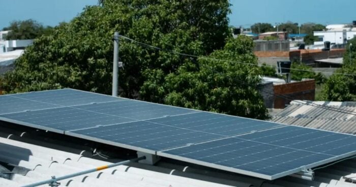Paneles solares instalados sobre un techo con árboles verdes y un horizonte suburbano en el fondo—probablemente un conjunto residencial de energía solar. - El Parque Solar DSE Neiva estrena la primera licencia ambiental exprés en la que se empeñó la ministra Irene Vélez