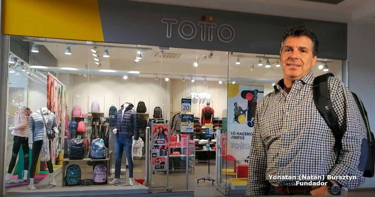 Man with a backpack standing outside a clothing store window display of jackets and backpacks, storefront sign reads 'TOI TOI'. - La historia detrás de la batalla de Totto por proteger su nombre