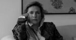 Black-and-white photo of a woman sitting on a sofa, resting her head on her hand, wearing a patterned blazer. - Desde Oriente llegó una historia de hombres y dioses