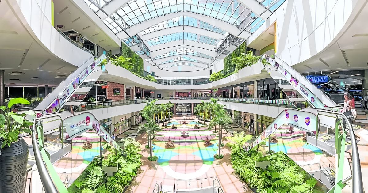Bright multi-level shopping mall atrium with escalators, glass ceiling, and tropical plants to create a sunny, open feel. - Ni Unicentro ni Plaza Central: este centro comercial de Medellín fue el que más dinero movió en Colombia