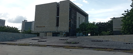 Front view of a modern stone university building with tiered concrete steps and trees nearby on a cloudy day. - Tres constructoras que lograron levantar el Museo de Arte Moderno de Barranquilla