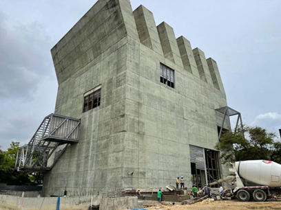 Concrete fortress-style building under construction with crenellated top, metal exterior stairs, a cement mixer truck nearby, and workers on the site. - Tres constructoras que lograron levantar el Museo de Arte Moderno de Barranquilla