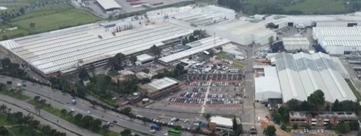 Aerial view of a large industrial complex with white-roof warehouses, a busy parking lot, and surrounding roads and greenery. - Por qué la Superfinanciera le cayó con millonaria multa a Chevrolet en Colombia, empresa que estrena director