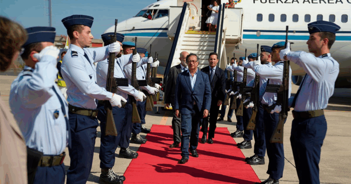 Con viaje a Roma, Petro se despide del FAC 001 que tanto aprovechó Dignitary in a blue blazer walks the red carpet as uniformed guards salute on both sides, with a plane in the background. - Con viaje a Roma, Petro se despide del FAC 001 que tanto aprovechó