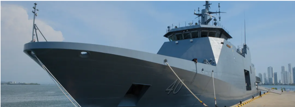 Un capitán de la armada está detrás del diseño los patrulleros oceánicos que Colombia quiere venderle a Uruguay Grey naval destroyer docked at a pier with a city skyline in the distance. - Un capitán de la armada está detrás del diseño los patrulleros oceánicos que Colombia quiere venderle a Uruguay