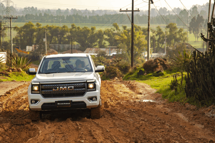 White GMC pickup driving on a muddy rural dirt road with power lines and cacti along the roadside, in a countryside setting. - Poder diésel sin pagar una fortuna: la JMC Grand Avenue llega para conquistar el trabajo pesado en Colombia