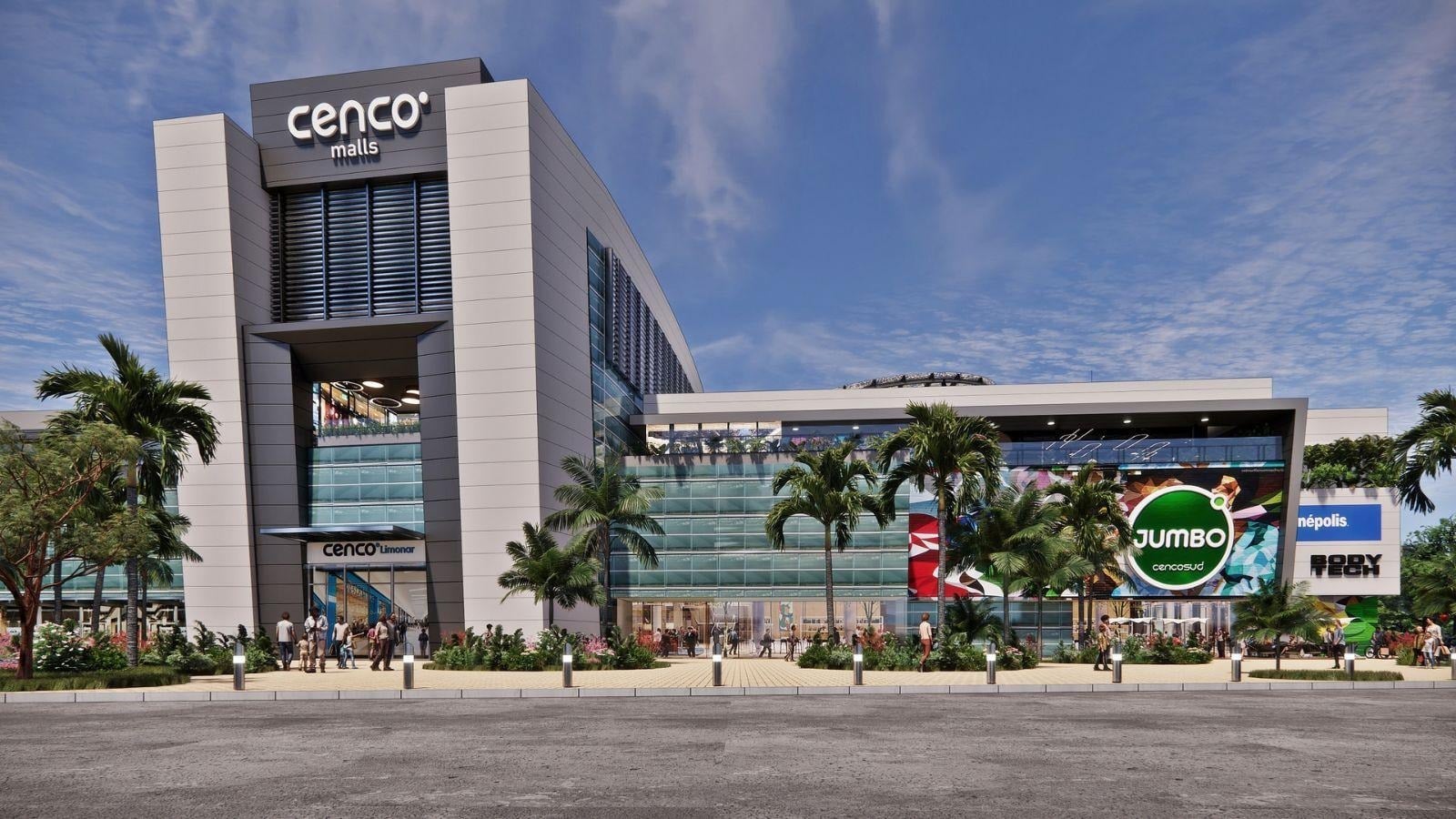Exterior view of a modern mall labeled 'cenco malls' with palm trees and a large Jumbo banner on the right under a blue sky by the entrance. (informative) - La apuesta de los chilenos de Cencosud para poner a competir su centro comercial en Cali contra los grandes