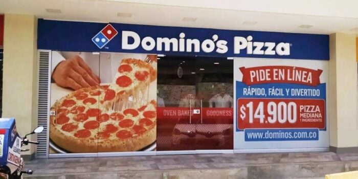 Después de 10 años, la cadena Archie’s vuelve a manos colombianas Domino’s Pizza storefront with a giant pepperoni pizza image on the doors and a large online‑order banner. - Después de 10 años, la cadena Archie’s vuelve a manos colombianas