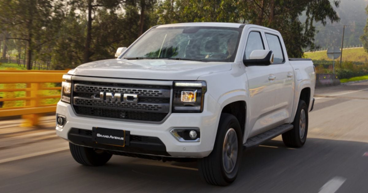 White GMC pickup truck driving on a two-lane road with an orange guardrail and green hills in the background in daylight. - Poder diésel sin pagar una fortuna: la JMC Grand Avenue llega para conquistar el trabajo pesado en Colombia