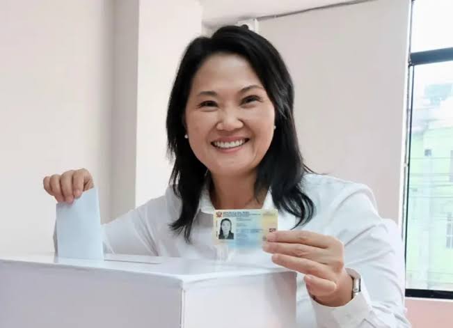 Smiling woman casts a ballot into a white ballot box at a polling station, holding her ID card. - Abelardo de la Espriella fue el último de una cadena de presidentes de derecha elegidos en América Latina