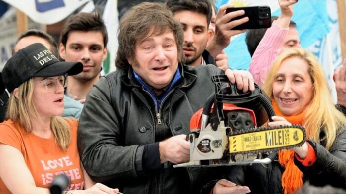 Man in a black jacket grips a chainsaw prop labeled MILE 23 at a crowded outdoor event, flanked by smiling spectators including a woman in an orange shirt and another taking a photo. - Abelardo de la Espriella fue el último de una cadena de presidentes de derecha elegidos en América Latina