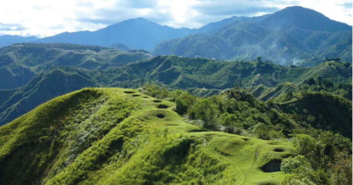 Green hillside with several circular hollows, leading to a valley and distant blue mountains under a partly cloudy sky - El tesoro escondido del Cauca que pocos se atreven a visitar y que la Unesco declaró Patrimonio de la Humanidad