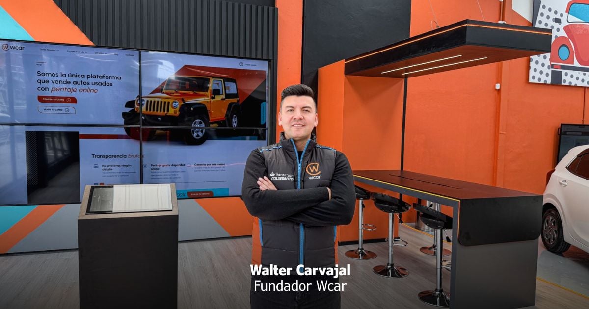 Portrait of Walter Carvajal, founder of Wcar, standing with arms crossed in a bright orange showroom with a long black-and-orange counter and screens in the background. - Con la plataforma Wcar, dos hermanos bogotanos se metieron al negocio de los carros usados en Colombia