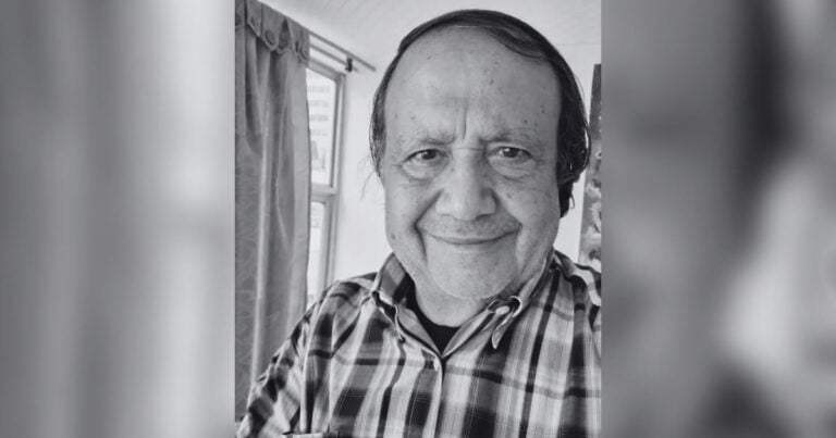 Black-and-white portrait of a smiling man in a plaid shirt indoors, facing the camera. - Ruinas de gobernantes despersonalizados