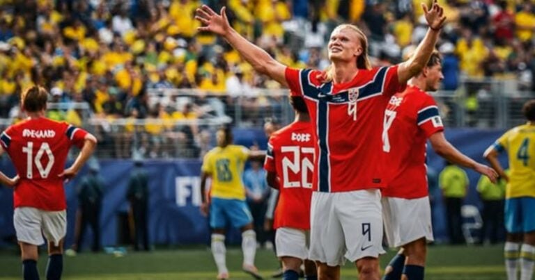 Las2orillas.co: Historias, voces y noticias de Colombia Soccer players in red uniforms celebrate on the field with arms raised as fans cheer in the stands; opponents in yellow in the background. - Las2orillas.co: Historias, voces y noticias de Colombia