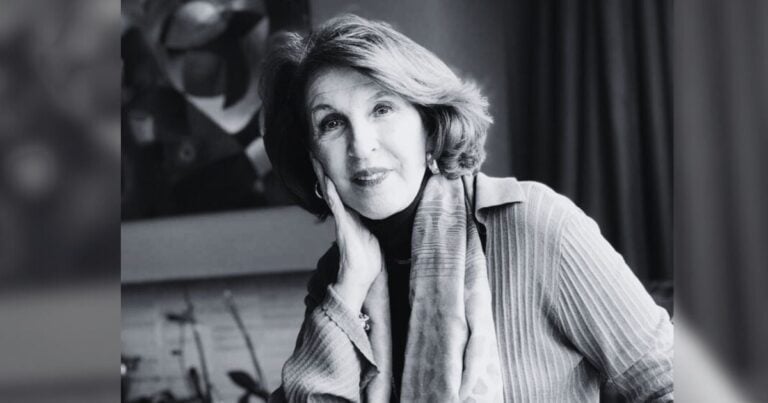 Black-and-white portrait of a smiling older woman resting her cheek on her hand, wearing a scarf and cardigan in a softly blurred setting. - Así es como las mascotas ayudan a criar mejores seres humanos