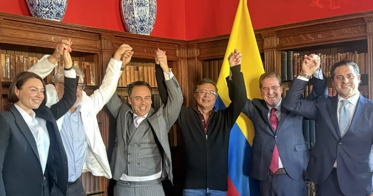 Six professionals in suits hold hands up in celebration in a wood-paneled room with a yellow-and-blue flag in the background. - Terminó sin resultados el contrato de  mil millones con abogados ingleses para sacar a Petro de la Lista Clinton
