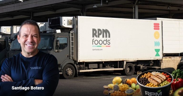 Las2orillas.co: Historias, voces y noticias de Colombia Smiling man in a dark blue shirt stands with arms crossed beside a large RPM Foods delivery truck; foreground shows fruit and a bowl of food. - Las2orillas.co: Historias, voces y noticias de Colombia