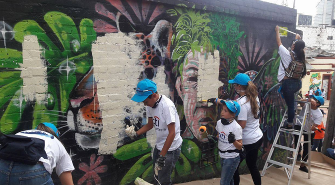 Un recorrido por las historias que el aerosol escribió en los muros de Bogotá: Grafiti Tour Group of children painting a colorful graffiti mural on a brick wall; some wear blue caps, including a kid on a ladder applying paint. - Un recorrido por las historias que el aerosol escribió en los muros de Bogotá: Grafiti Tour