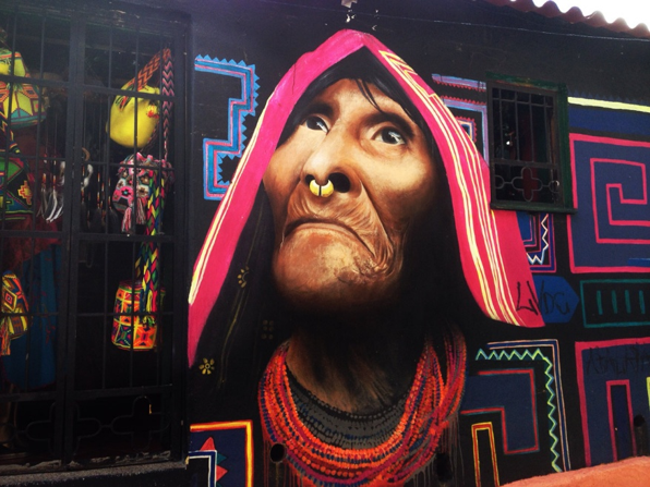 Un recorrido por las historias que el aerosol escribió en los muros de Bogotá: Grafiti Tour Mural of an elderly woman with a pink headscarf and nose ring, gazing upward, surrounded by bright geometric patterns. - Un recorrido por las historias que el aerosol escribió en los muros de Bogotá: Grafiti Tour