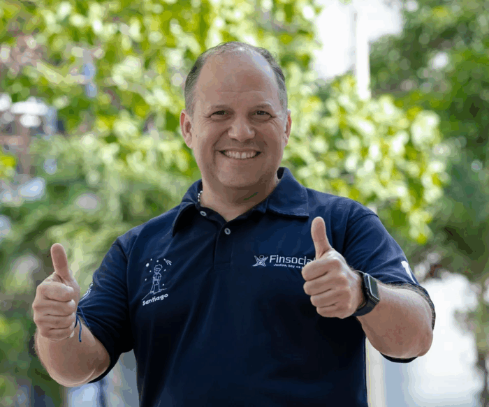 El negociazo con el que el empresario paisa Santiago Botero busca conquistar a EE. UU. Smiling man in a navy polo giving two thumbs up in a sunny outdoor garden with green foliage behind him. - El negociazo con el que el empresario paisa Santiago Botero busca conquistar a EE. UU.