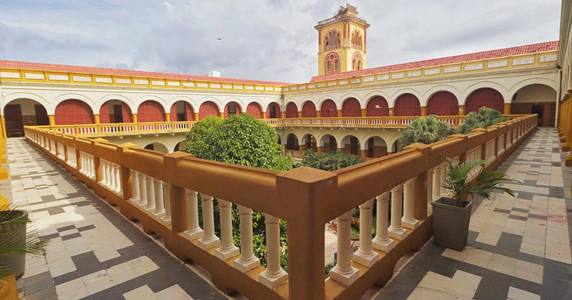 La pelea de mil millones que la Universidad de Cartagena le ganó a la poderosa Ecopetrol Inner courtyard of a colonial-style building with a central garden, orange-brown railing, and arched walkways surrounding it. - La pelea de mil millones que la Universidad de Cartagena le ganó a la poderosa Ecopetrol