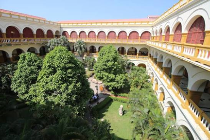 La pelea de mil millones que la Universidad de Cartagena le ganó a la poderosa Ecopetrol Interior courtyard with yellow arches and red accents surrounding a landscaped garden and palm trees. - La pelea de mil millones que la Universidad de Cartagena le ganó a la poderosa Ecopetrol