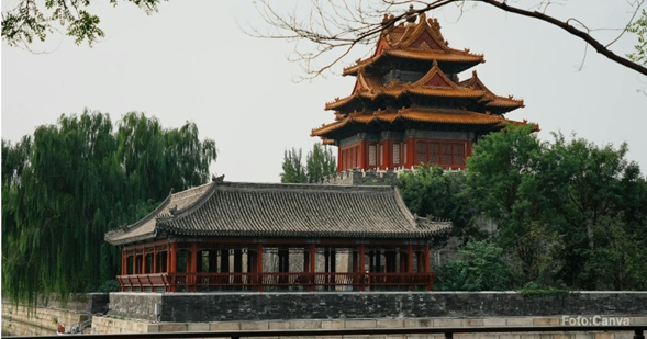 Red multi-tiered Chinese pagoda behind a traditional pavilion by a stone wall, surrounded by trees. - La empresa china que perdió el pulso con los centros comerciales tipo outlet