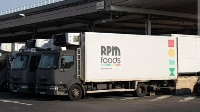El negociazo con el que el empresario paisa Santiago Botero busca conquistar a EE. UU. RPM Foods delivery truck parked at a loading dock under an overpass, with other trucks nearby. - El negociazo con el que el empresario paisa Santiago Botero busca conquistar a EE. UU.