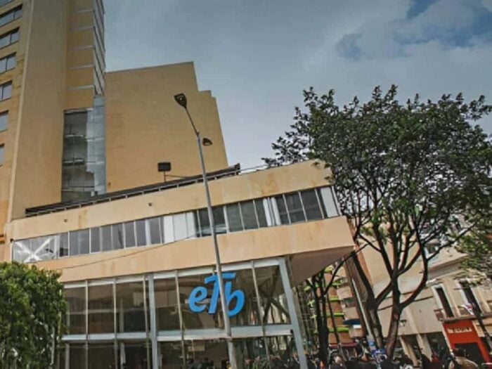 La buena nueva de Diego Molano después de un año y medio en la Presidencia de la ETB Modern glass-front building with a blue 'eb'/logo mark at street level, surrounded by trees and pedestrians on a city sidewalk. - La buena nueva de Diego Molano después de un año y medio en la Presidencia de la ETB