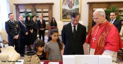 Las2orillas.co: Historias, voces y noticias de Colombia Catholic ceremony with a red-vested cleric and a man in a suit as two girls view items on a table. - Las2orillas.co: Historias, voces y noticias de Colombia