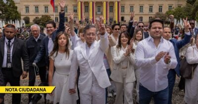 Group of people in white outfits raising hands and making peace signs during a public demonstration in front of a government building with Colombian flags in the background. - Las2orillas.co: Historias, voces y noticias de Colombia